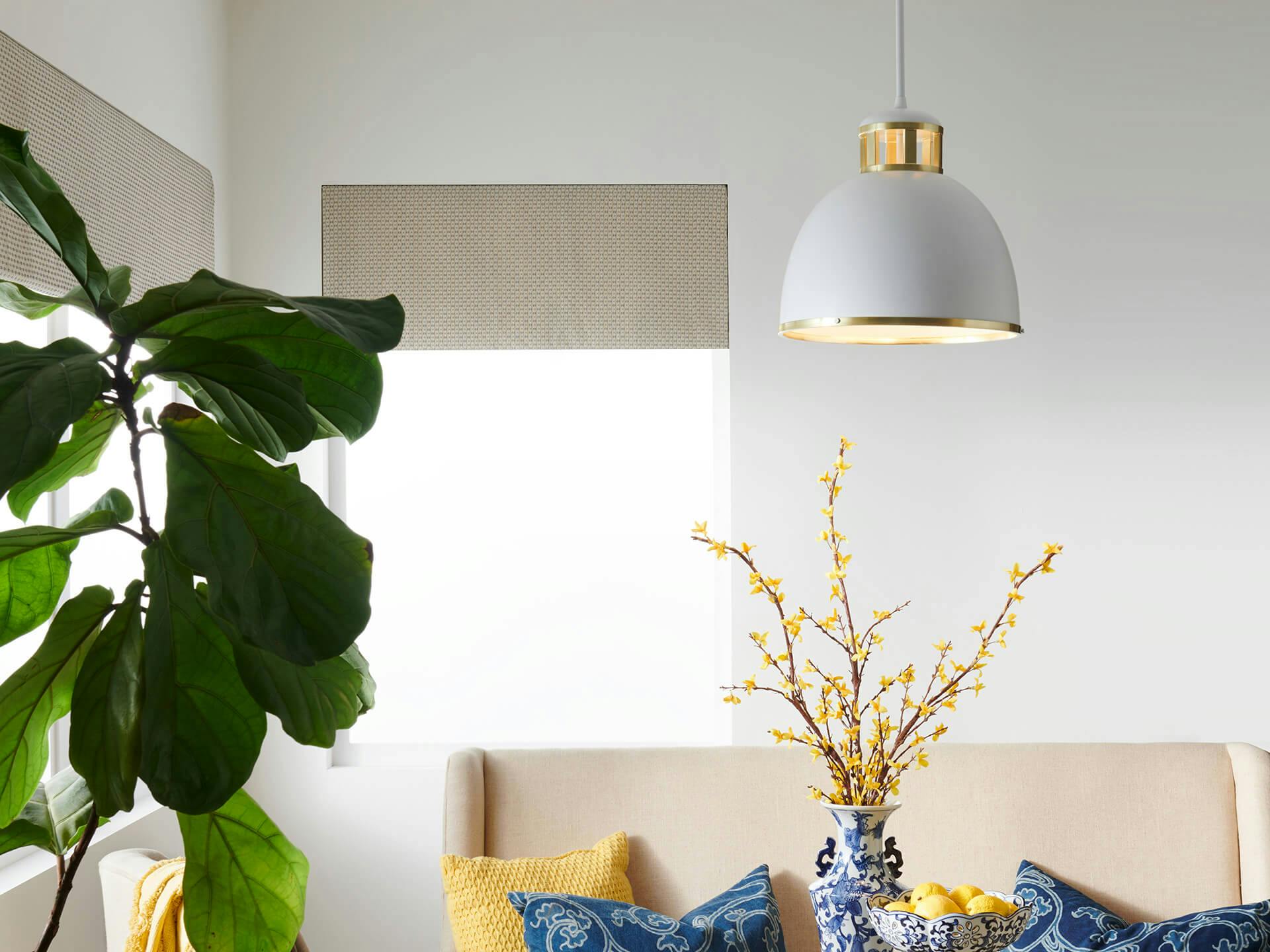 Bright living room with cream color couch, blue and yellow pillows, plant and featuring a Sansara gold and white pendant lamp
