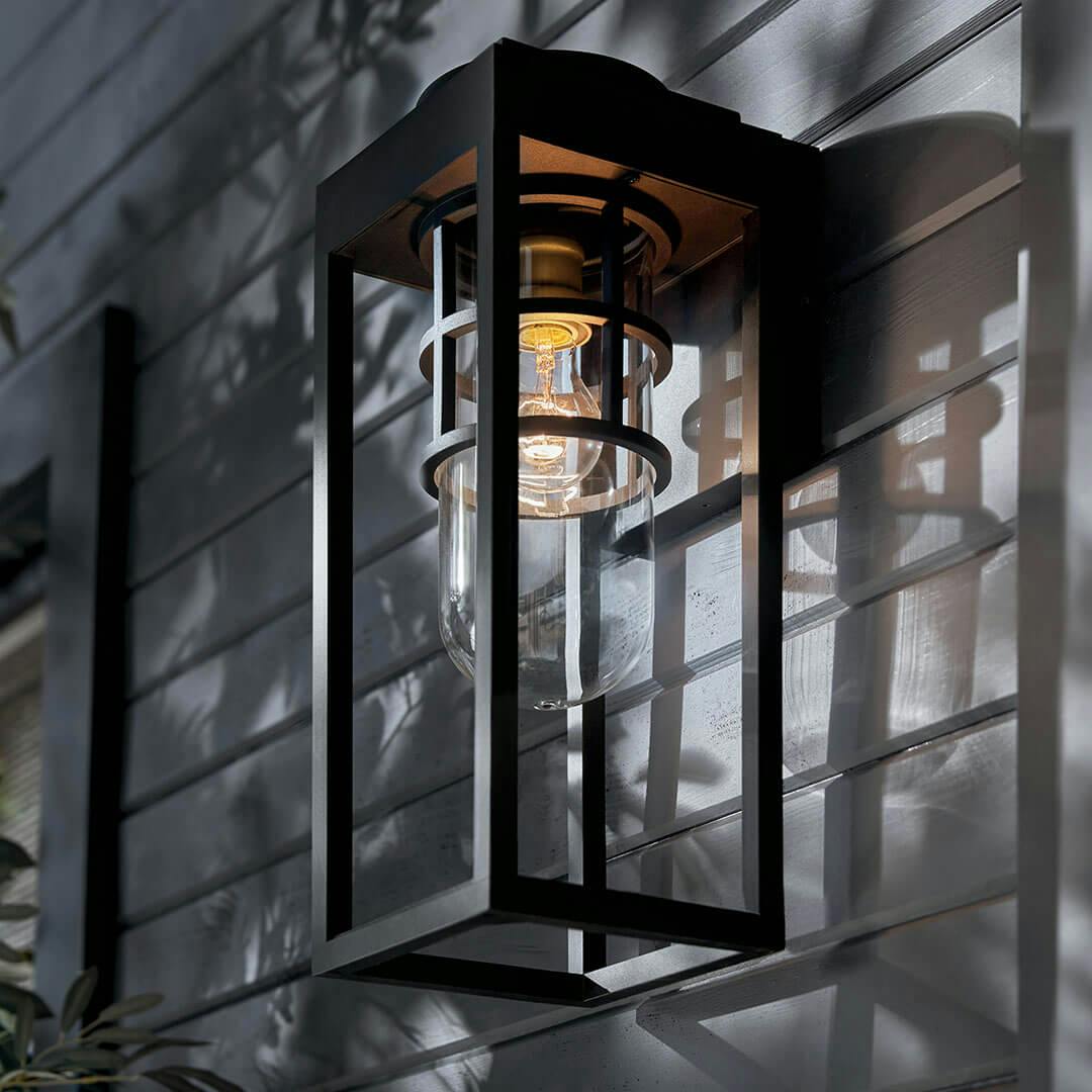 Patio at dusk with the Hone 18" 1 Light Outdoor Wall Light with Clear Glass in Textured Black with Natural Brass Accent