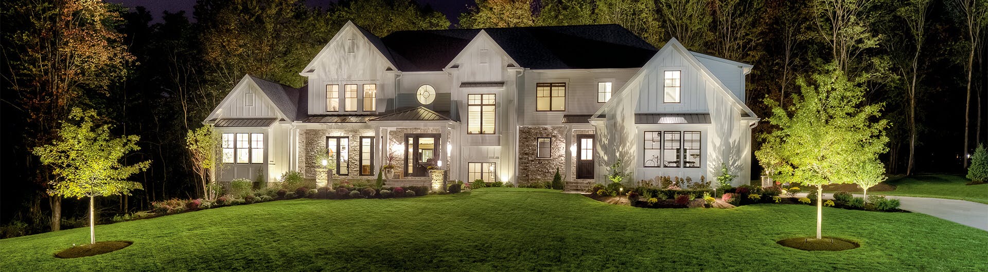 Modern farmhouse front exterior landscape lit up with different outdoor landscape lights at night 