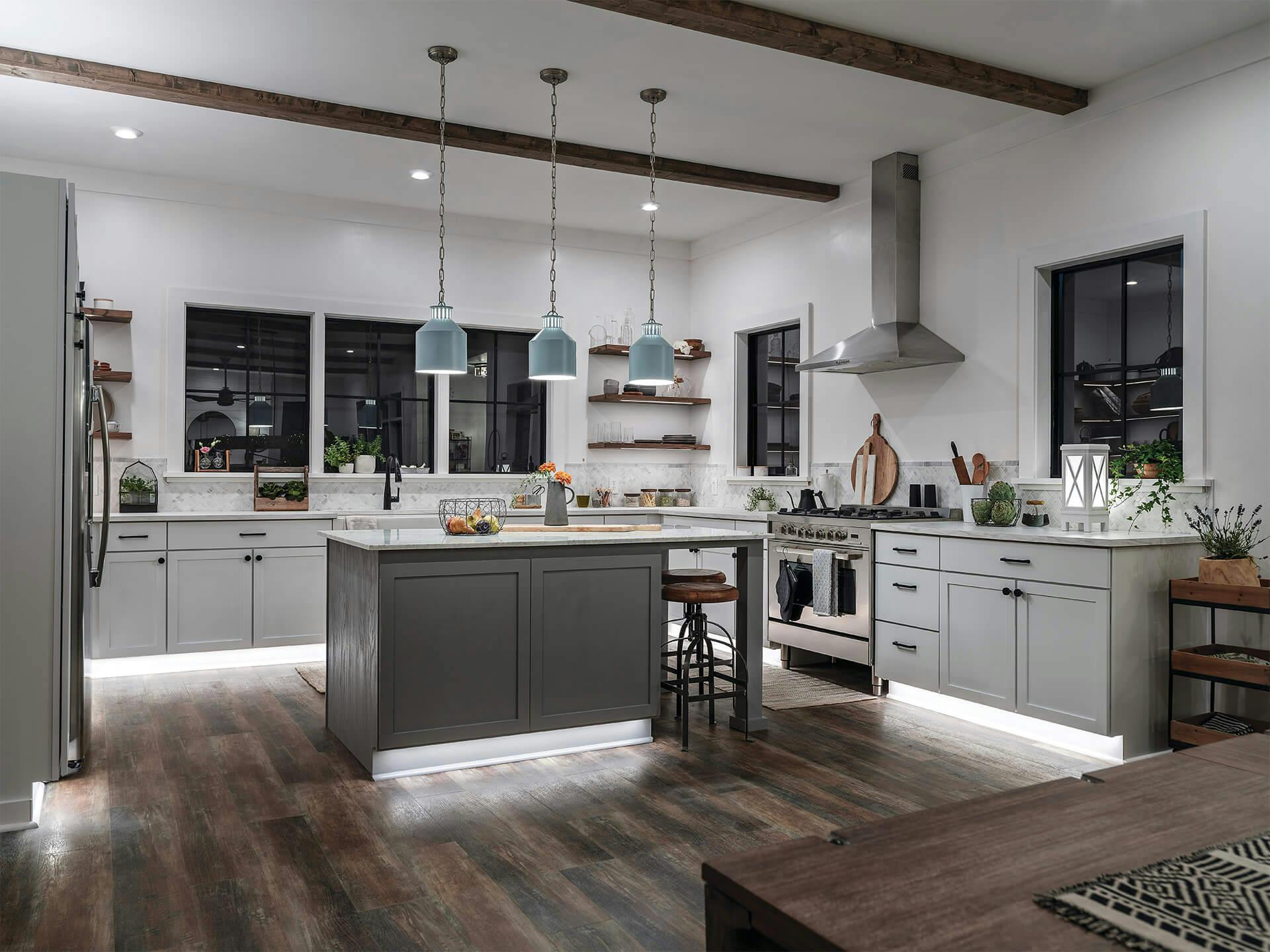 Kitchen with three lit Montauk pendants in light blue with a Farmhouse Montego Lantern Style Lamp on the countertop and Under Cabinet Lights throughout