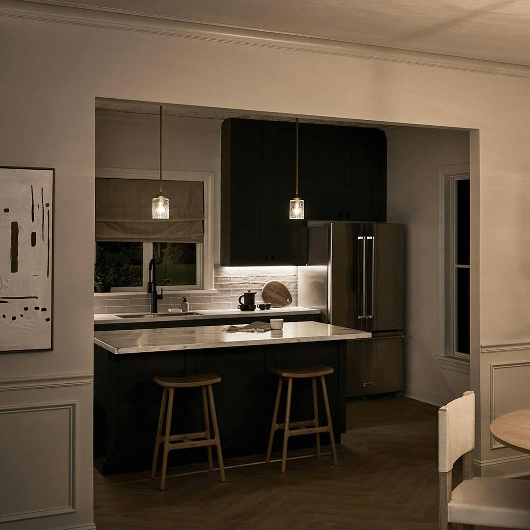Kitchen at night with the Winslow 7.5" 1-Light Mini Pendant Light with Clear Seeded Glass in Natural Brass