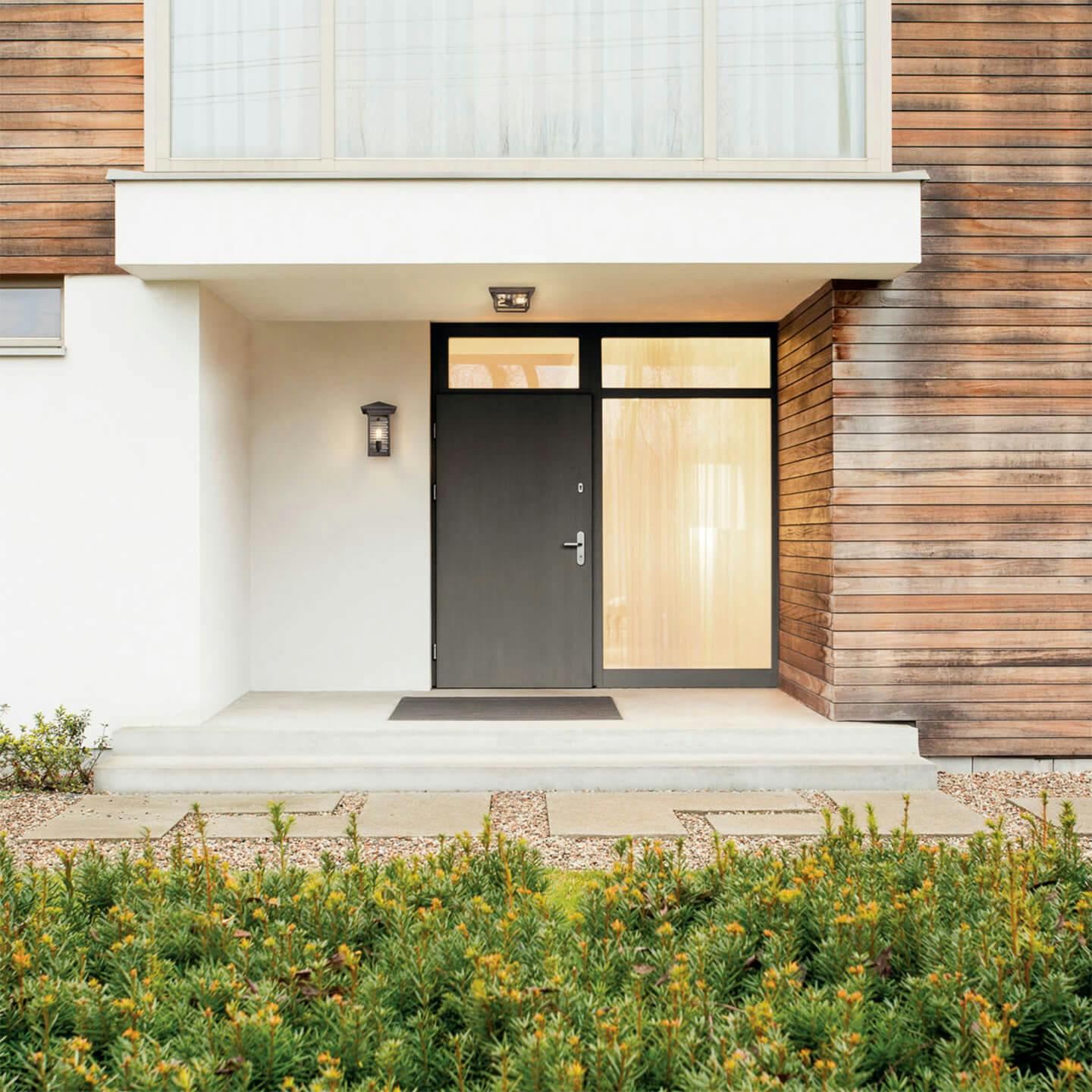 Exterior image of a front entrance of a modern house with concrete and wood finishes with Wayland exterior wall light next to the front door and a Wayland flush mount above the entry way 