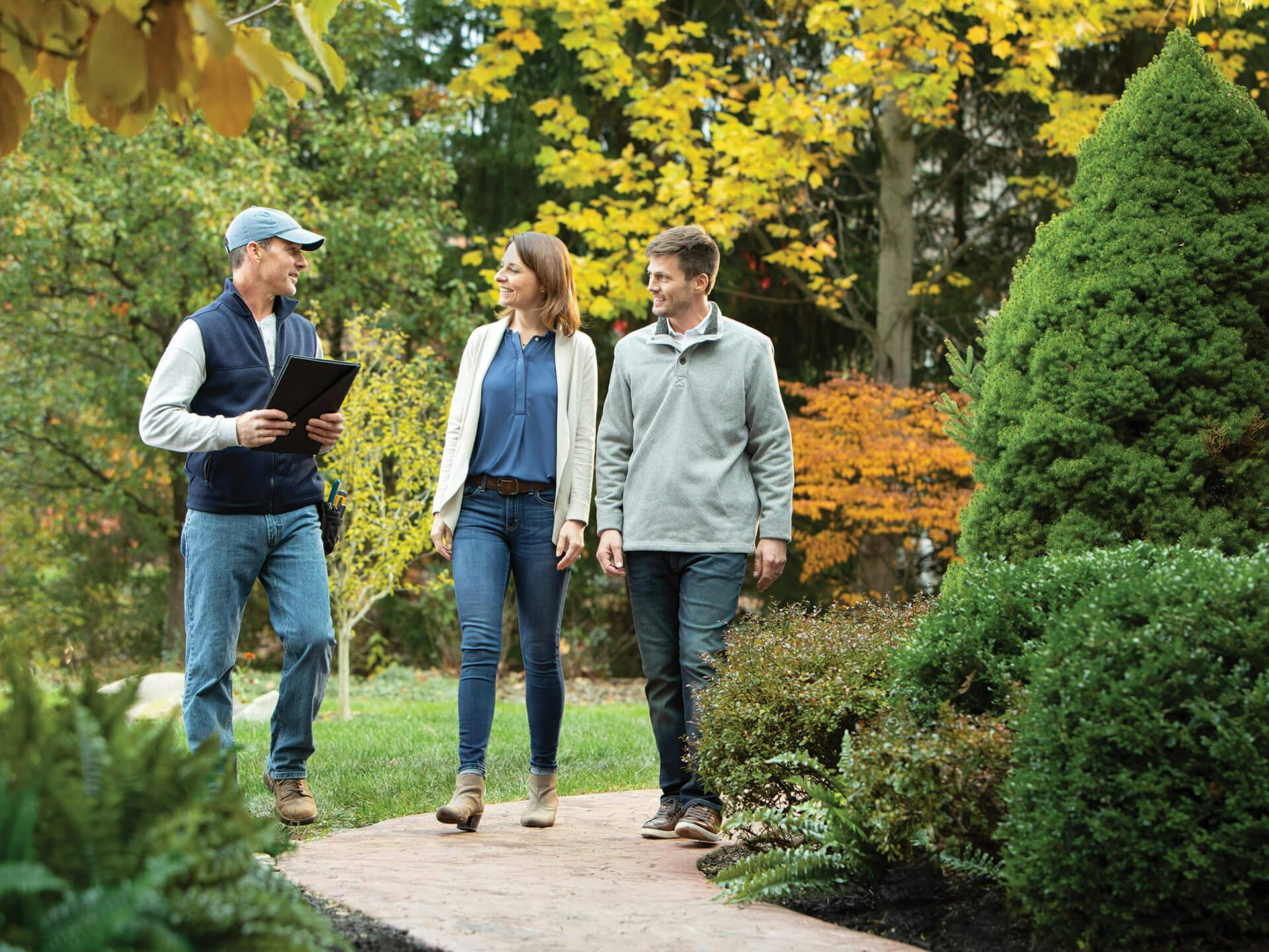 Man with clipboard walking on an outside garden path with a smiling couple