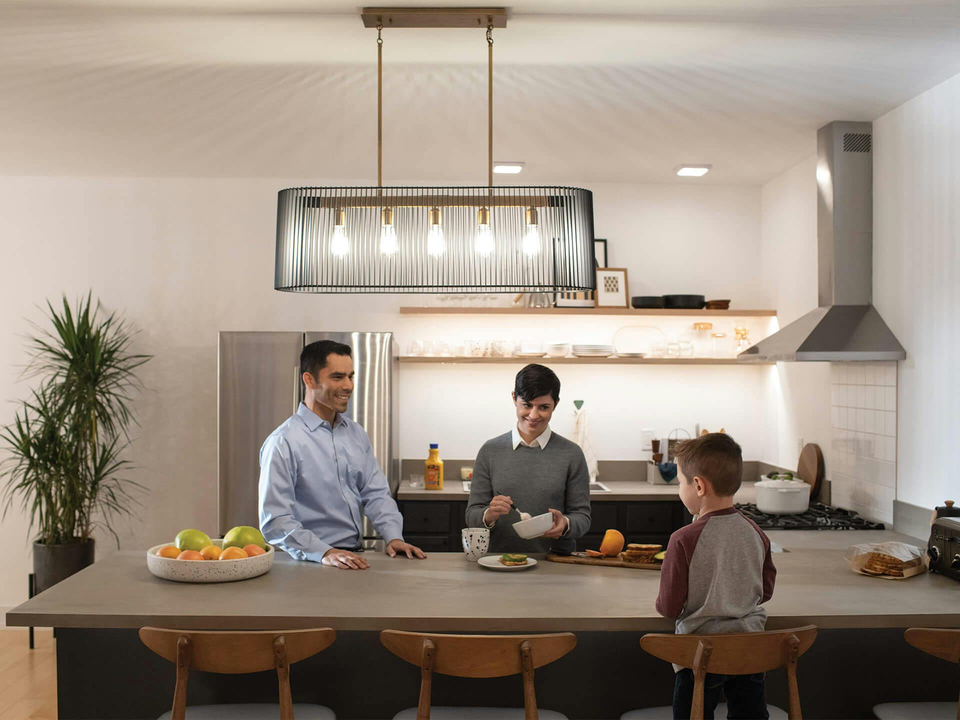 Kitchen with a family preparing breakfast on the island while a lit Linara chandelier hangs above with Zeo ceiling lights in the background