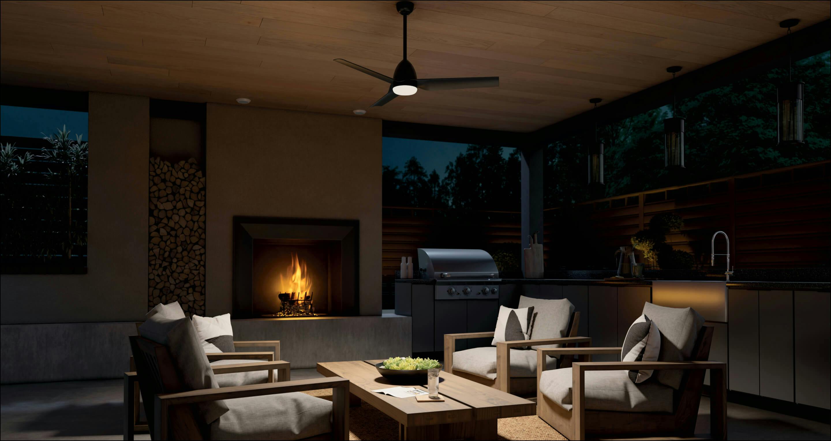 Outdoor kitchen at night lit only by a Fit ceiling fan in the center of the room and the fireplace