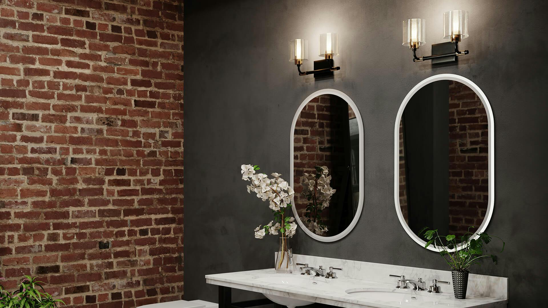 Bathroom at nighttime featuring two Menillo mirrors with a lit Harvan sconce above each against a dark gray wall 