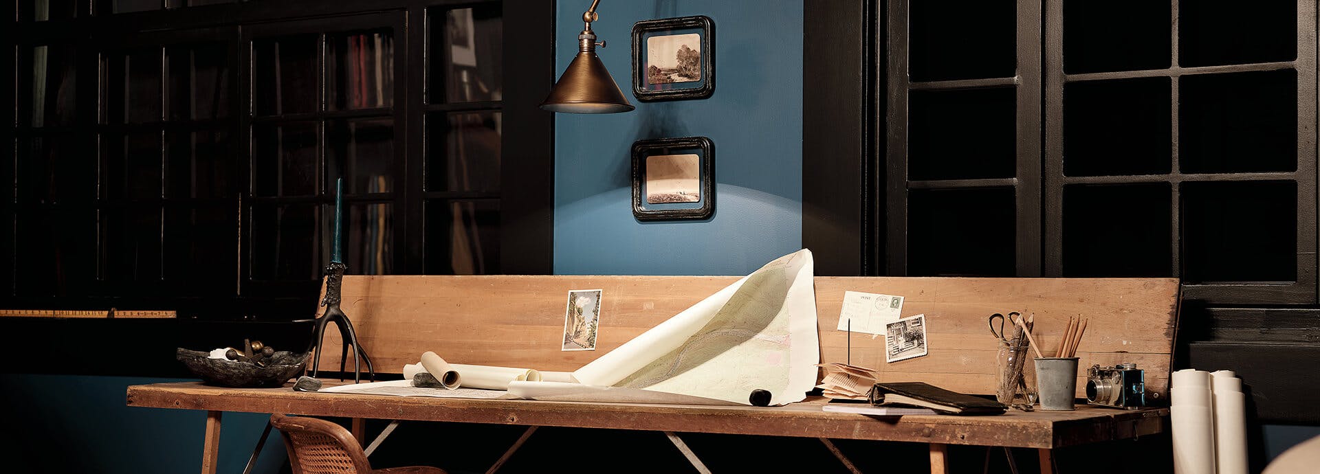 Den at night with a sconce hanging above a workbench with a scroll of paper and variety of writing tools