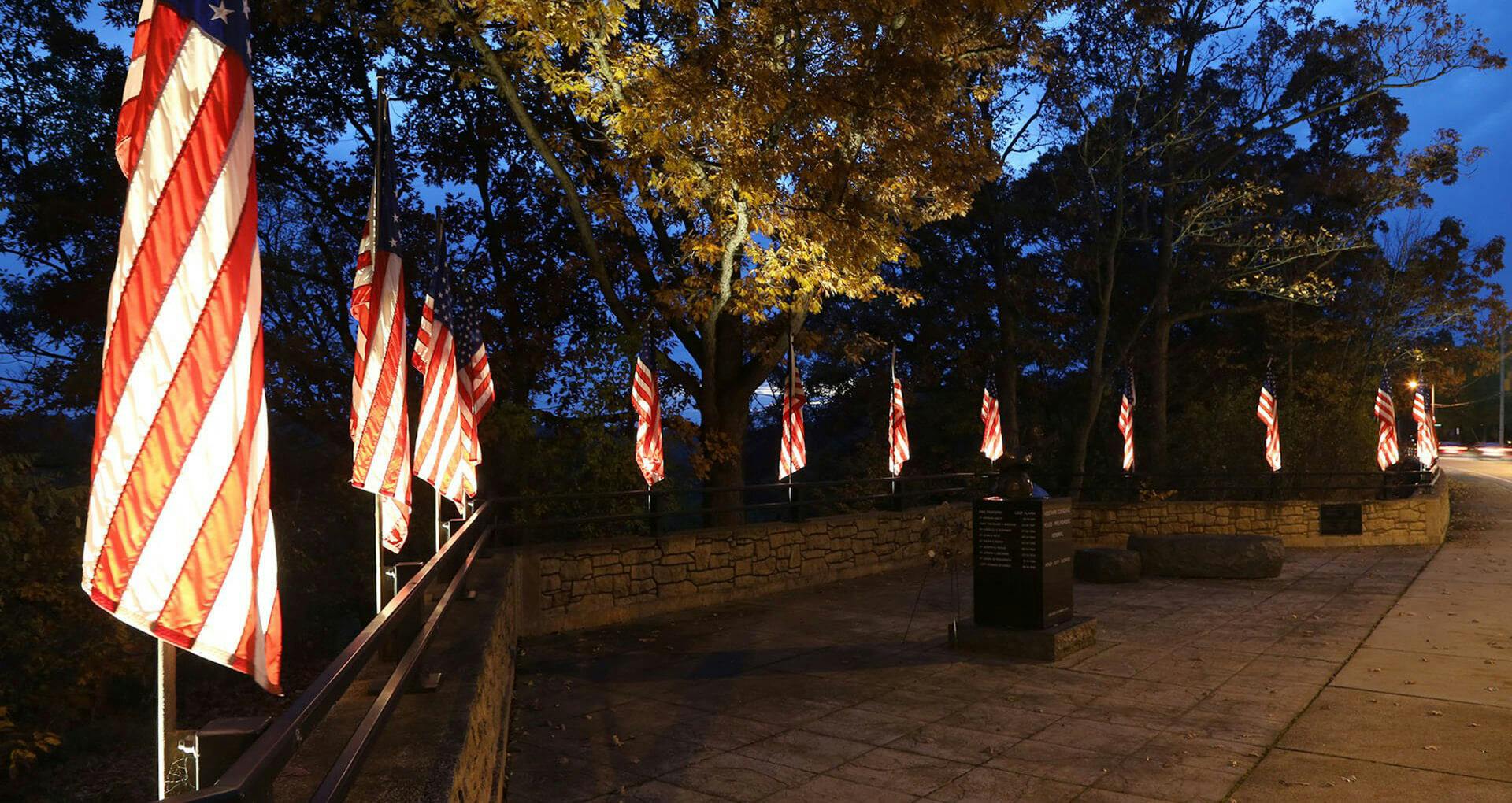West Park memorial at night with several American flags hanging and features uplighting on each