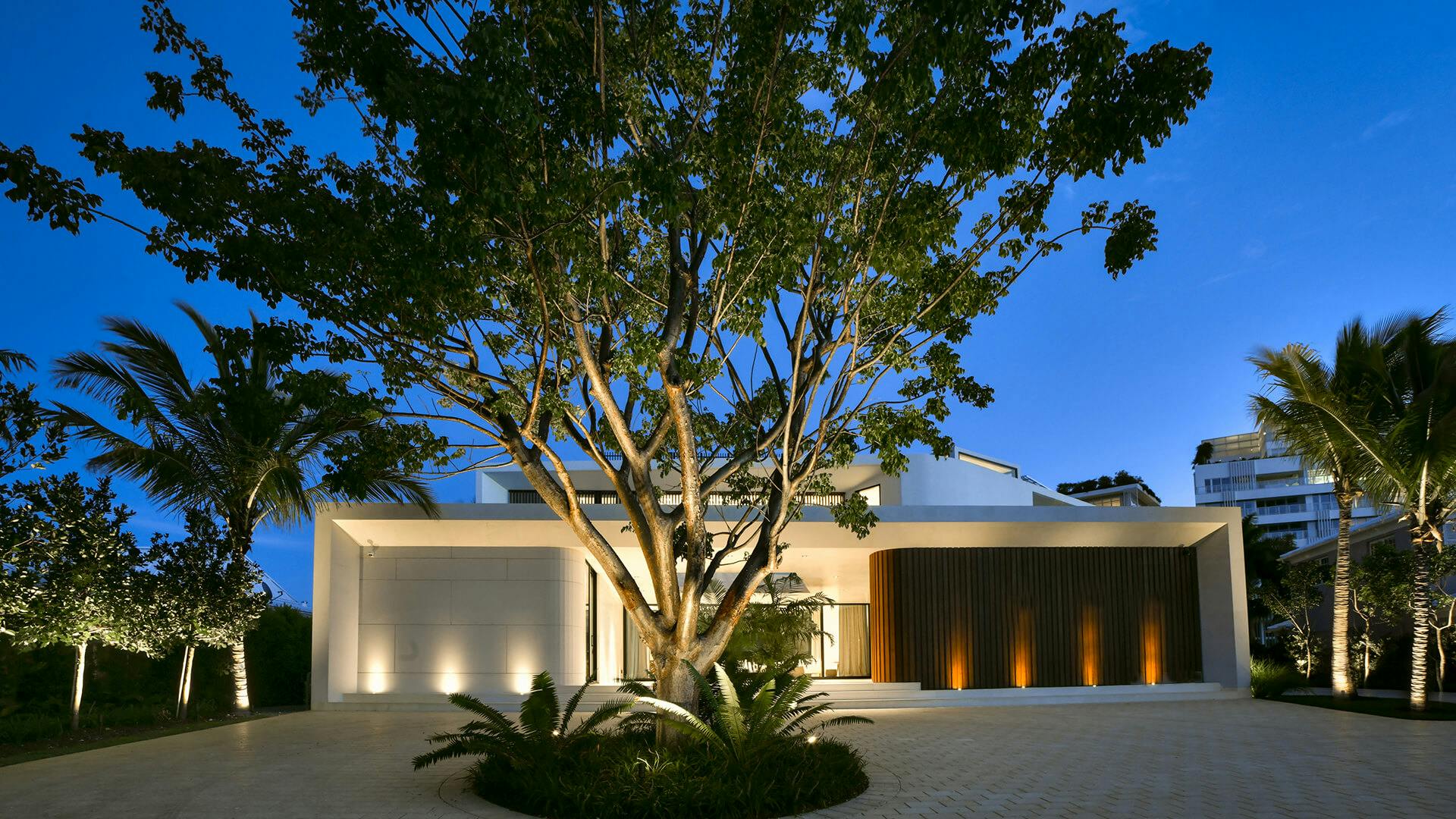House exterior at dusk with center tree lit by landscape lighting 