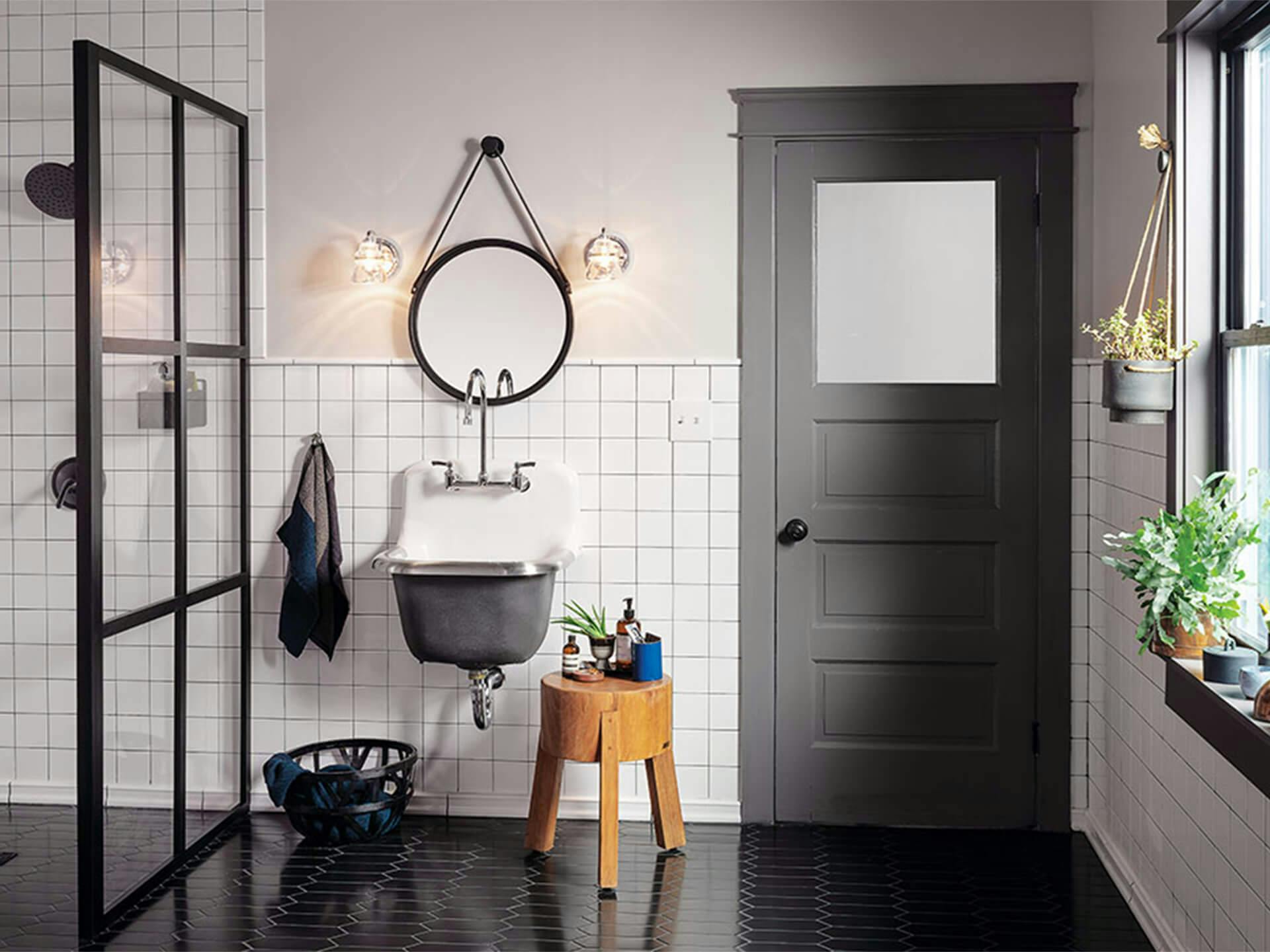 A modern bathroom with Talland vanity lights on either side of a mirror above an industrial bathroom sink turned on during the day