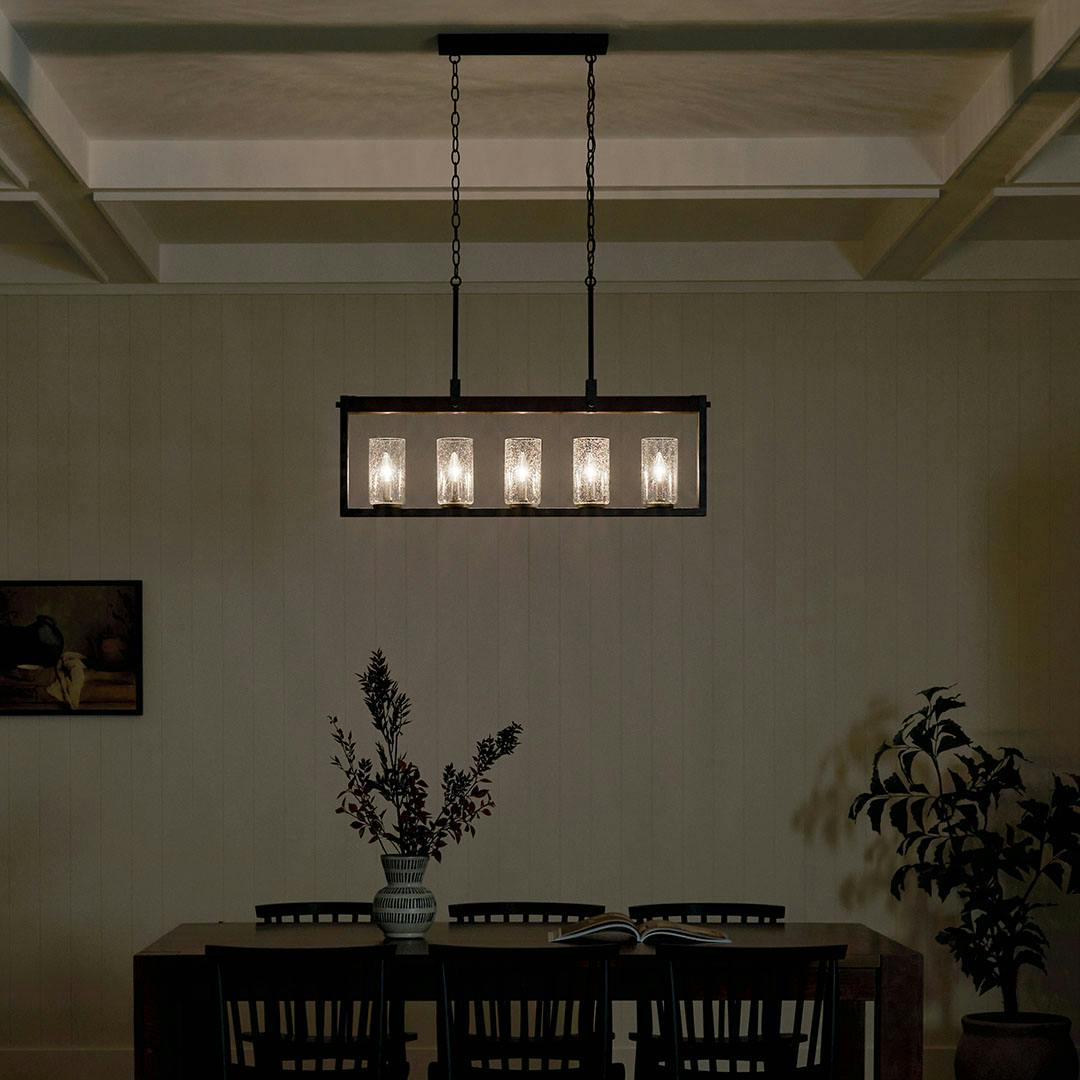 Dining room at night with the Barrington 5 Light Linear Chandelier in Distressed Black and Auburn Wood Tone