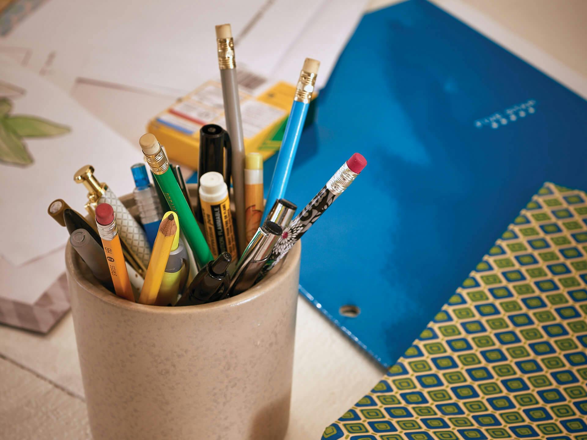 A cup of pencils and two colored folders sit amongst papers on a table