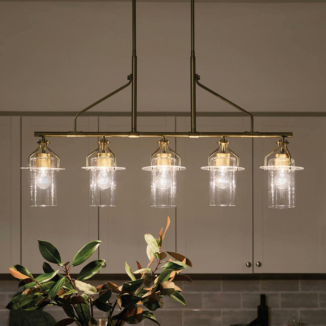 Night time kitchen with Everett 42 Inch 5 Light Linear Chandelier with Clear Glass in Natural Brass
