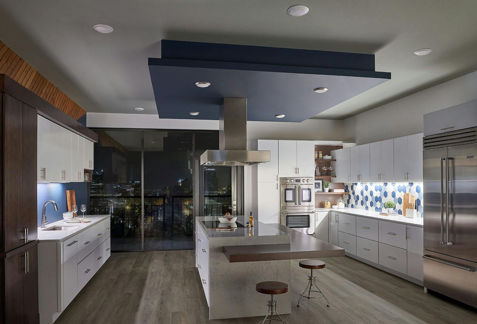 Modern white kitchen with blue, wood, and stainless steel accents in an urban setting with only under cabinet lighting turned