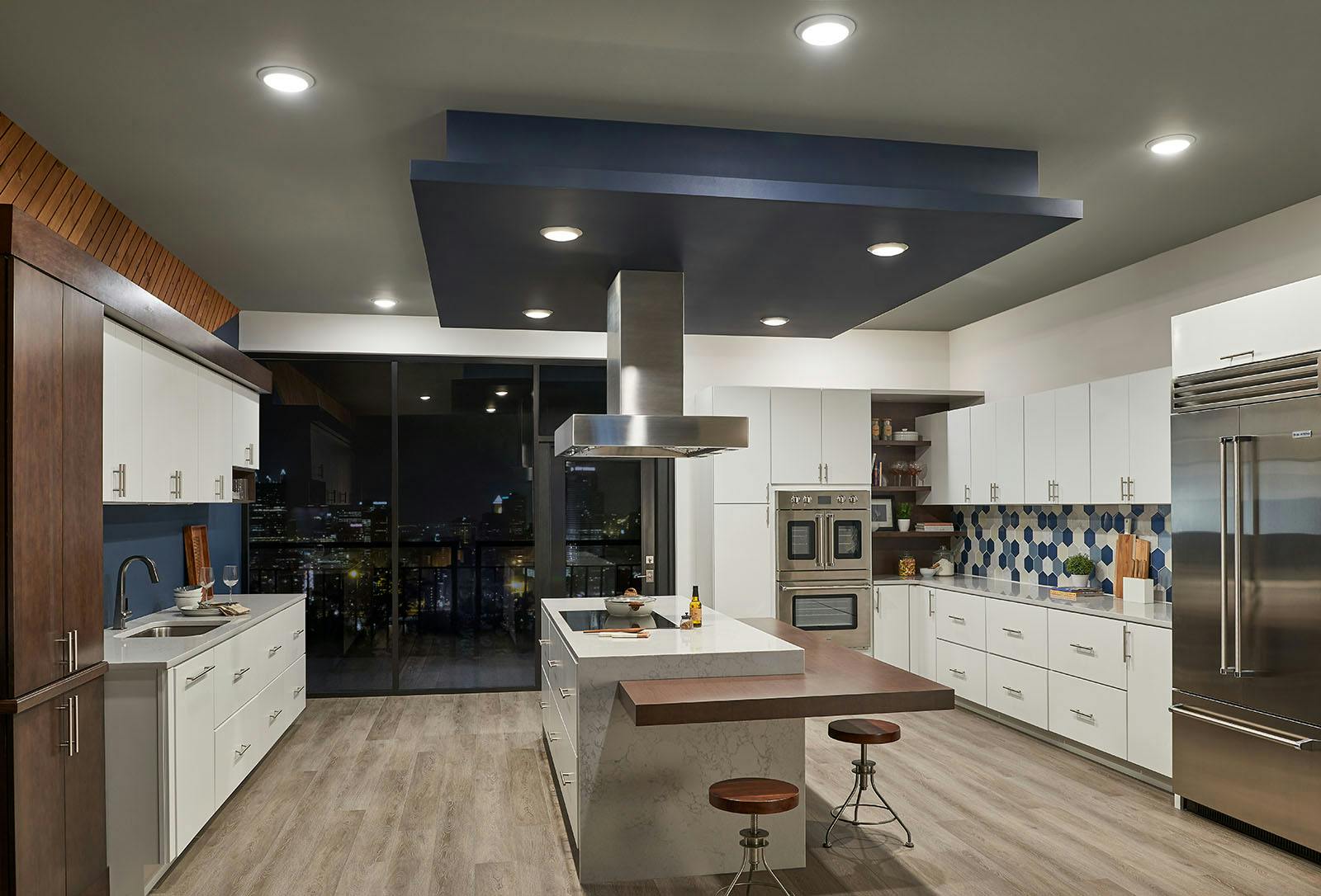 Modern white kitchen with blue, wood, and stainless steel accents in an urban setting with only downlights turned on