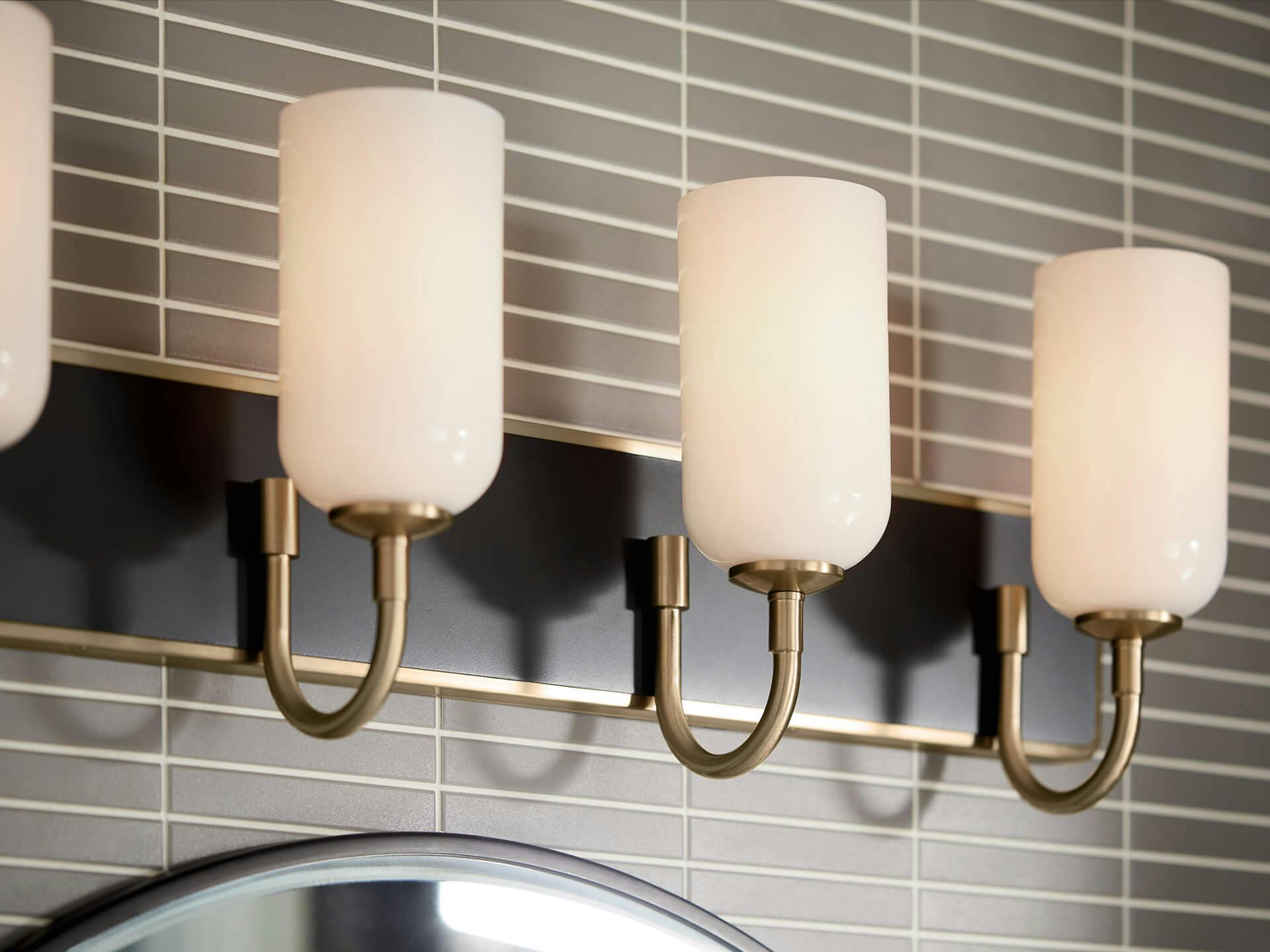 Close-up of a Solia vanity light in champagne bronze hanging above a bathroom mirror