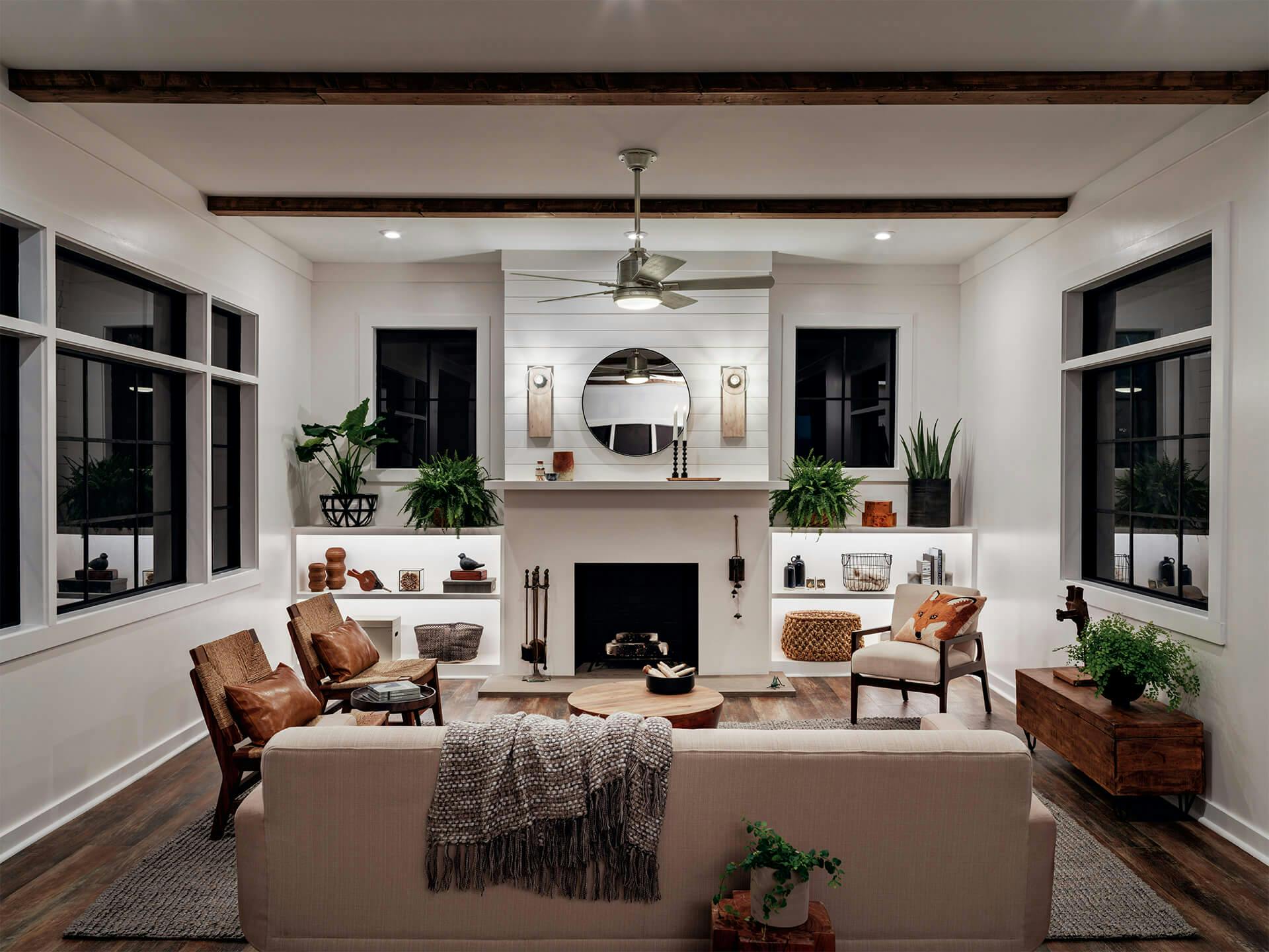 A living room lit up by a Colerne ceiling fan, Marquee sconces on the back wall, and flush mounts, all turned on during the night 