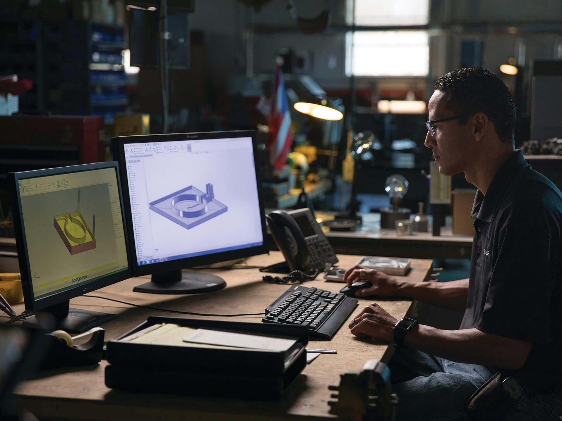 Man working at a desk in workshop space with a 3D model on his monitors
