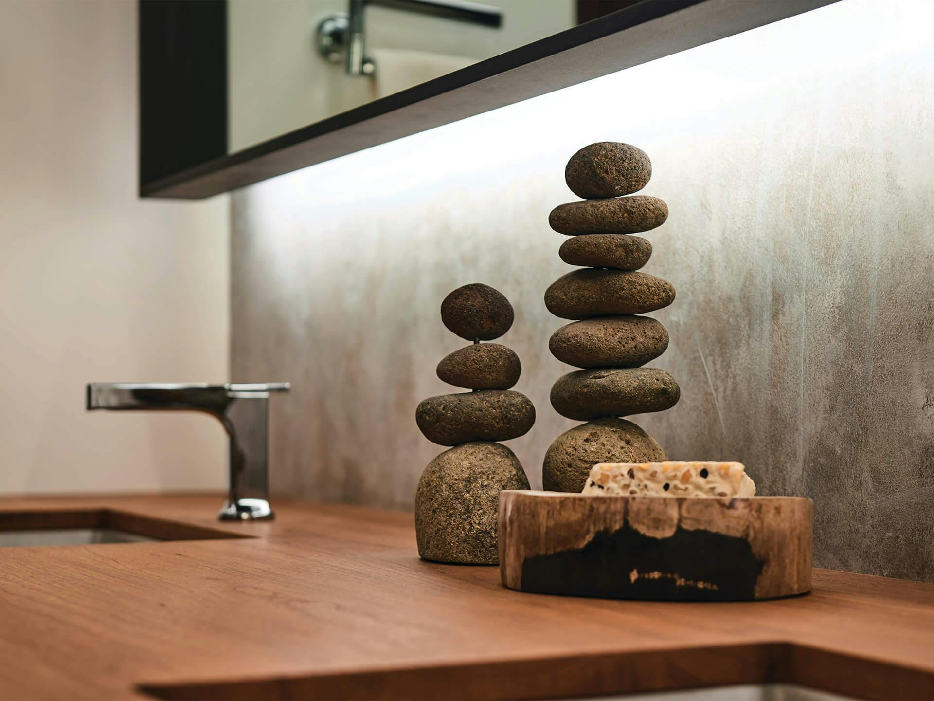 Lifestyle image of stacked stones on wooden bathroom countertop. 