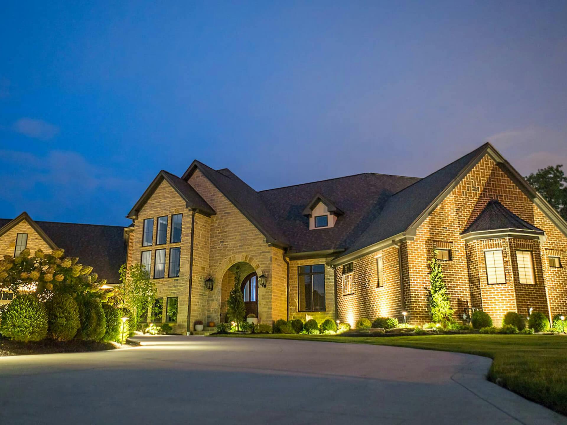 Exterior landscape of a large brick home with variety of uplighting