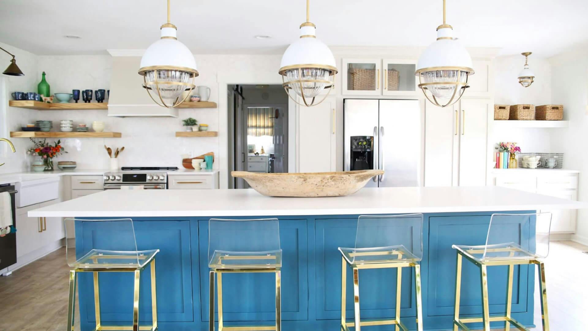 White kitchen with long blue kitchen island with three pendant lights in gold and white finish hanging above.
