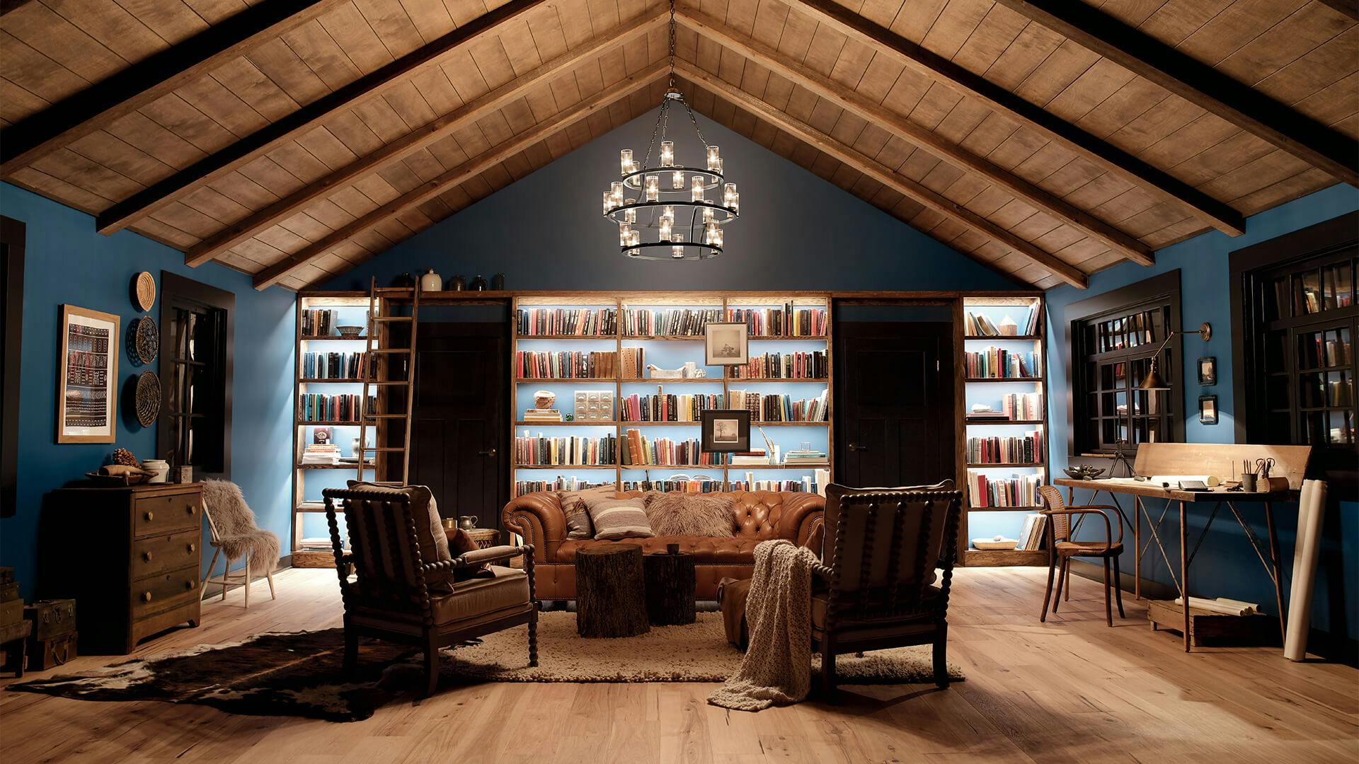 A south western style library den lit up by a Mathias chandelier with tapelights lighting up the book shelves on the back wall at night