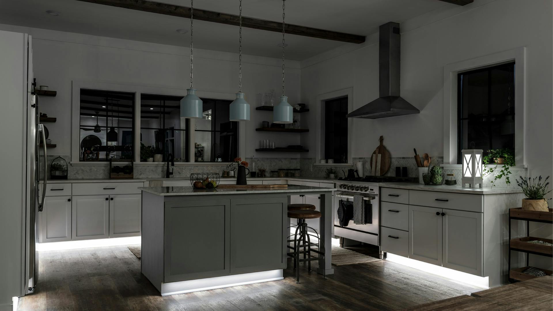 A kitchen with tape lights and Montauk pendants with just the kick toe lighting on at night 