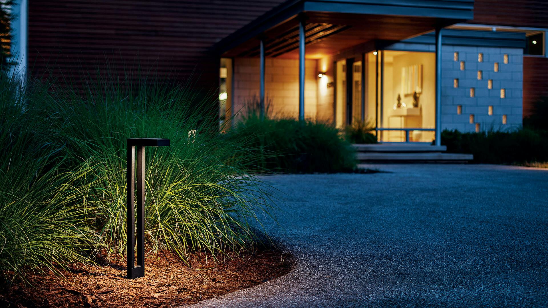 A contemporary path light illuminates part of a residential landscape with a house in the background