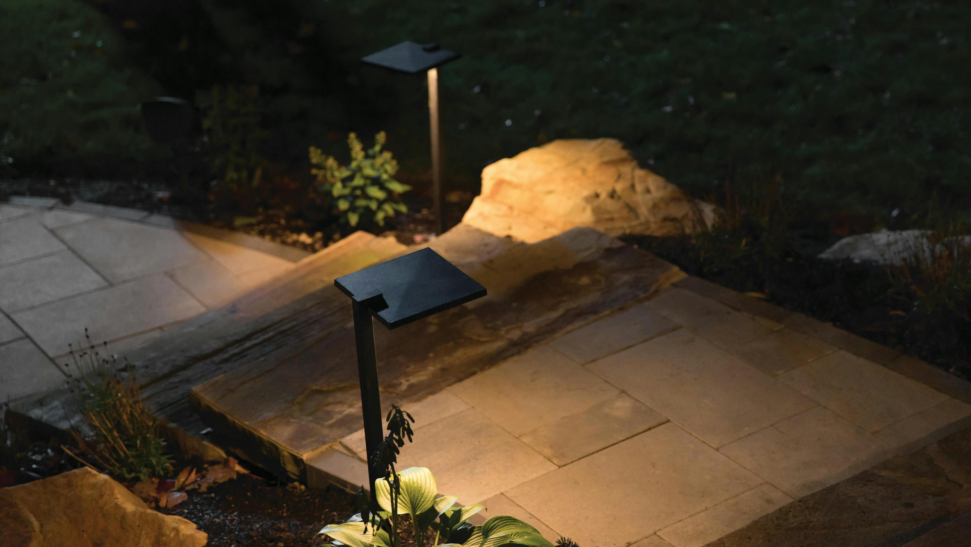 Black textured path light lighting up a stone path with landscaping