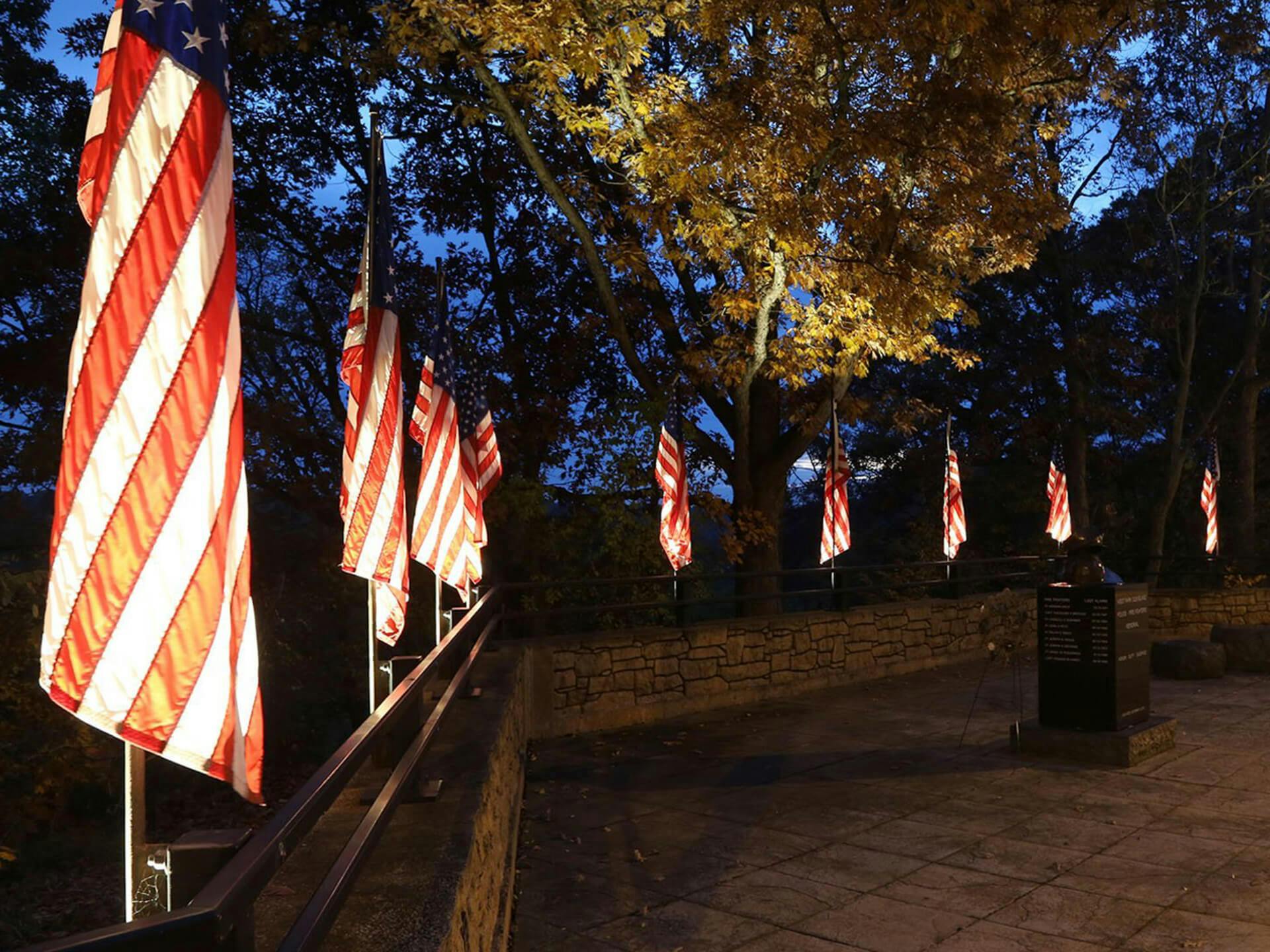 West Park memorial at night with several American flags hanging and features uplighting on each