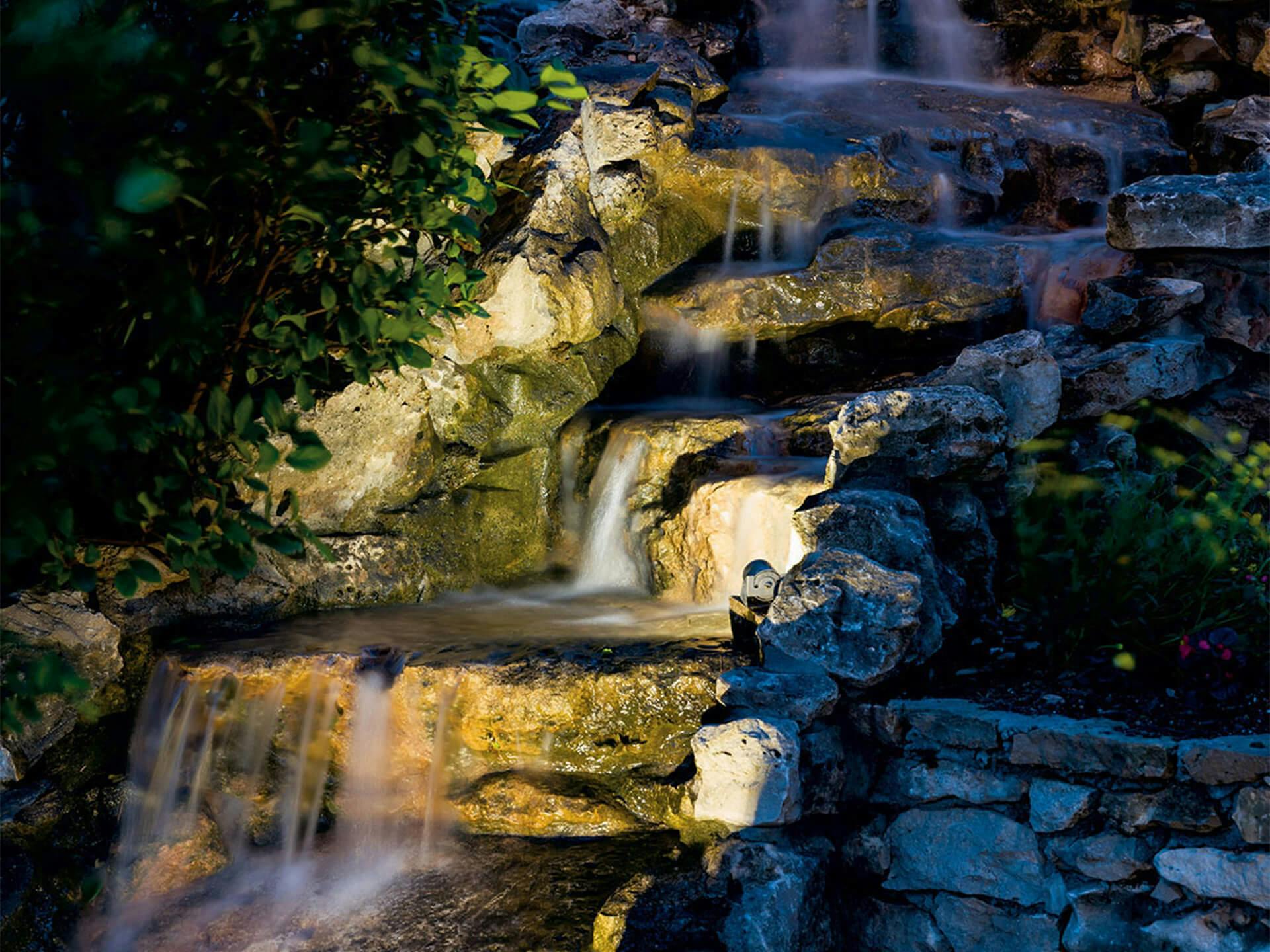 Small waterfall with uplighting highlighting its beauty