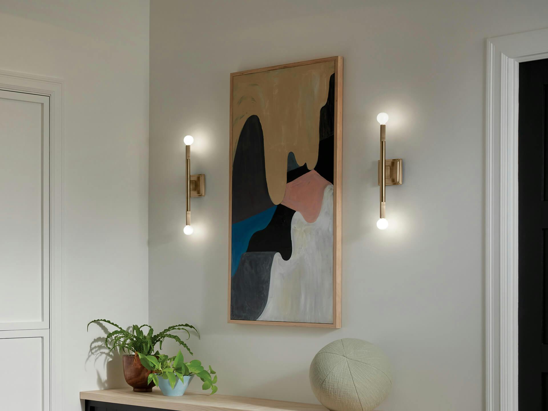 A hallway featuring two lit Sisu sconces in champagne bronze beside a painting