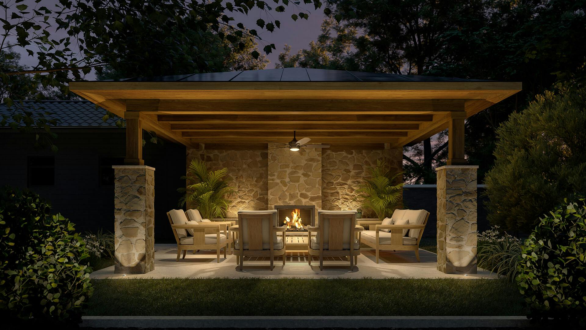Covered outdoor stone patio with wooden patio furniture and ground lights on at night