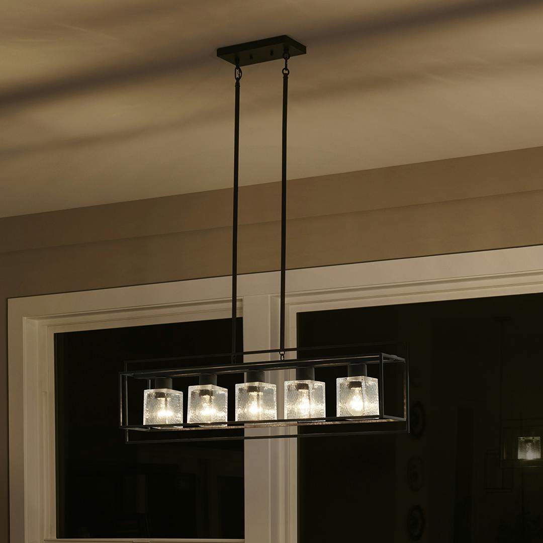 Night time dining room with Edinborough 5 Light Linear Chandelier in Textured Black with Clear Hammered Glass