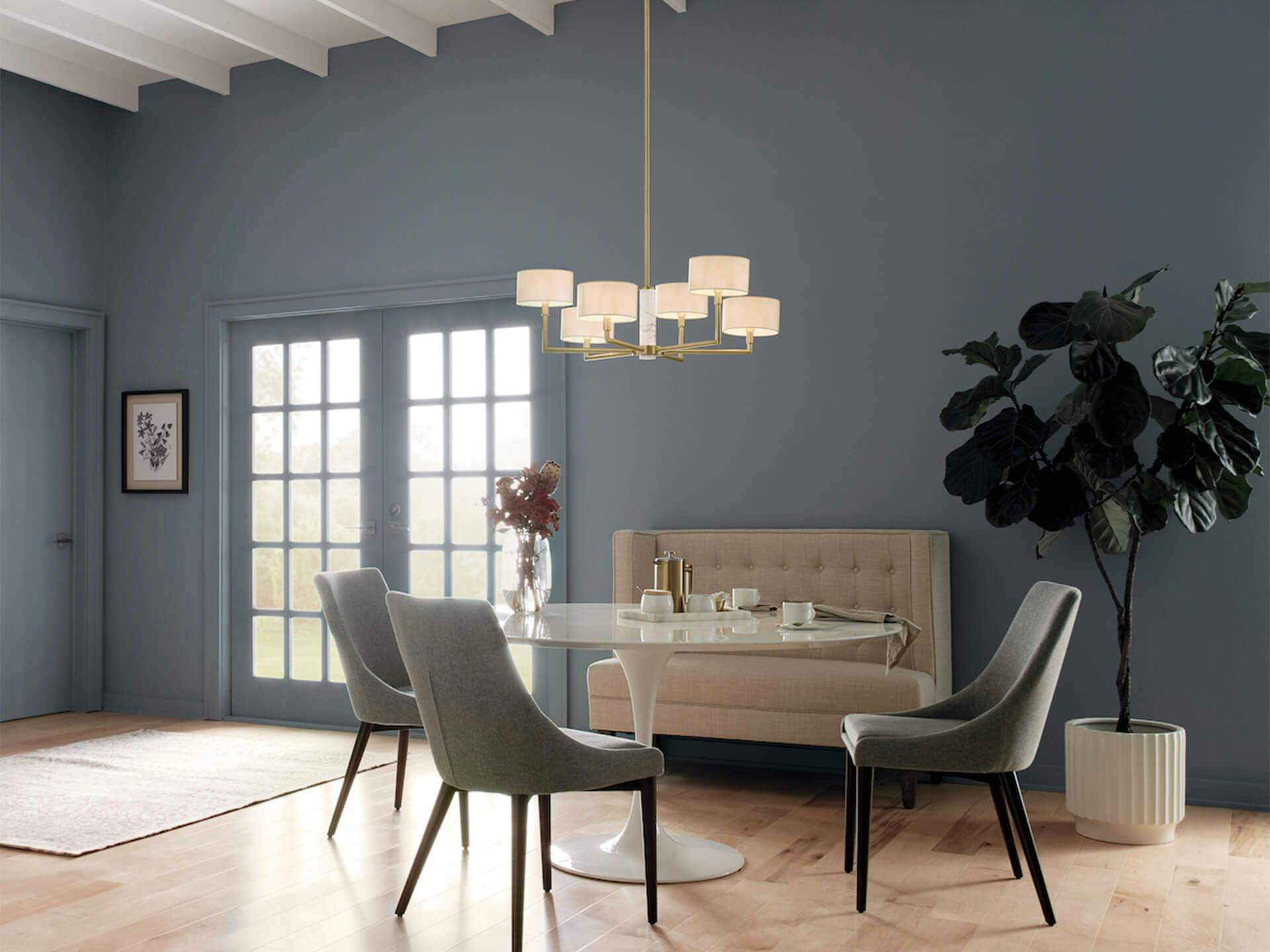 Dinning room with neutral blue paint wall lit with a 6 light shaded Laurent chandelier with a gold finish in the day 