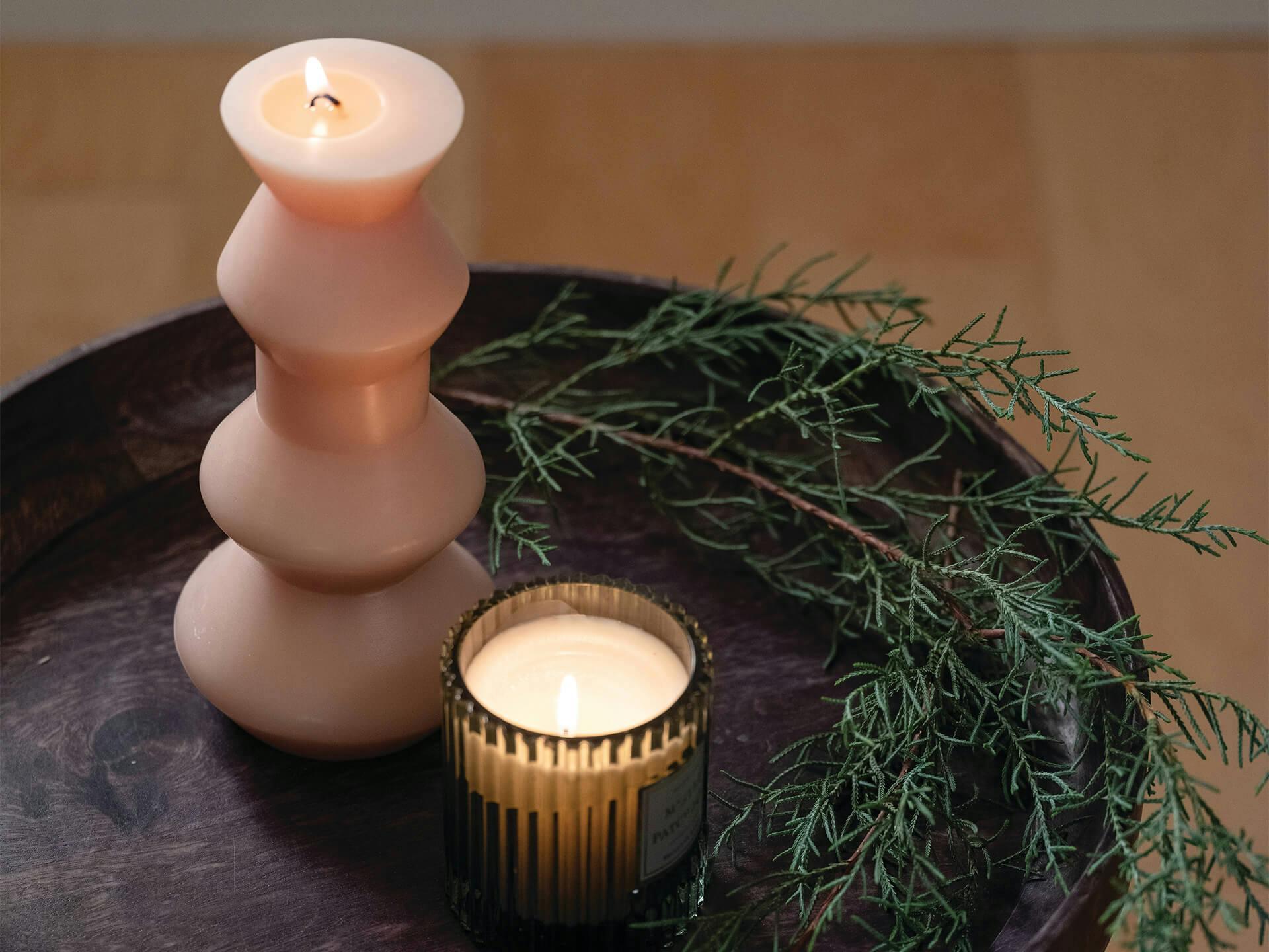 Lifestyle image of an end table decorated with two candles and some spruce tree leaves 