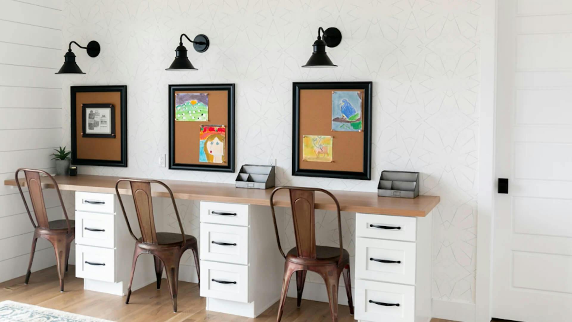 Long desk featuring three stations, each with a chair, drawer and cork board, with Northland sconces above them