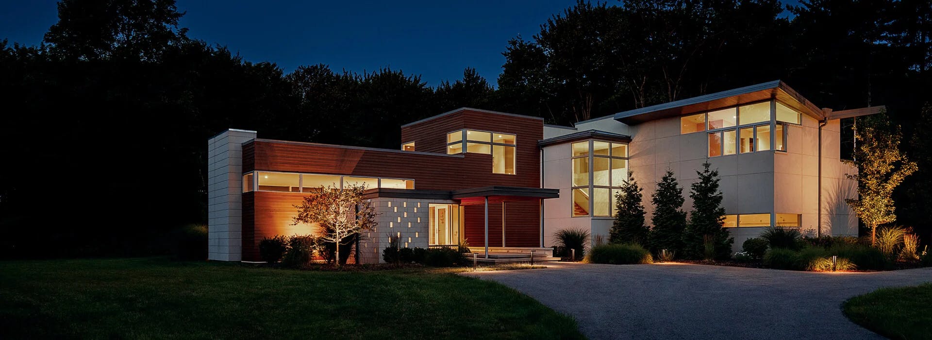 Exterior of a contemporary house at night alit with interior and exterior lights.