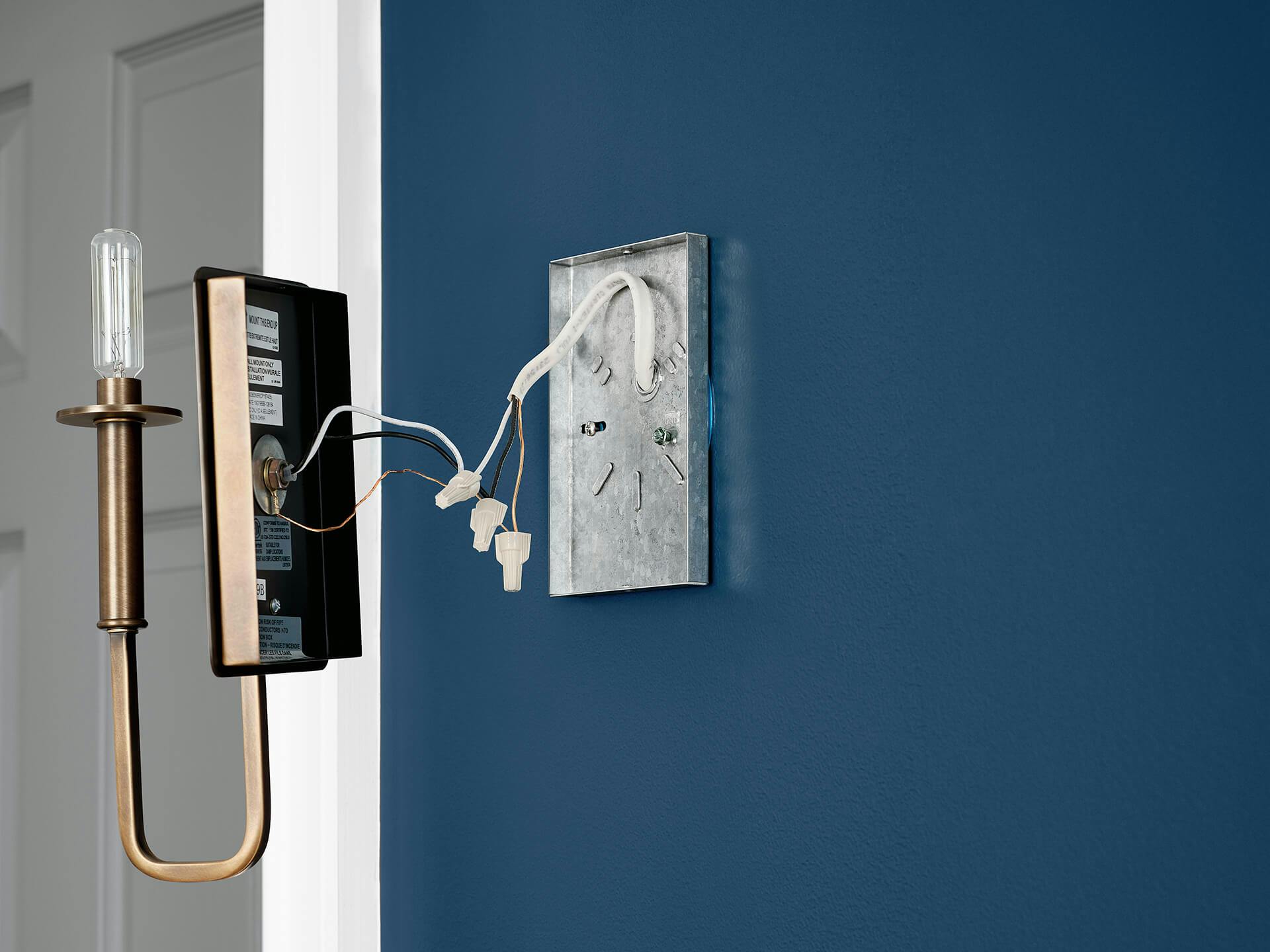 Blue wall with a brass alden sconce's wires connecting with the outlet box wires