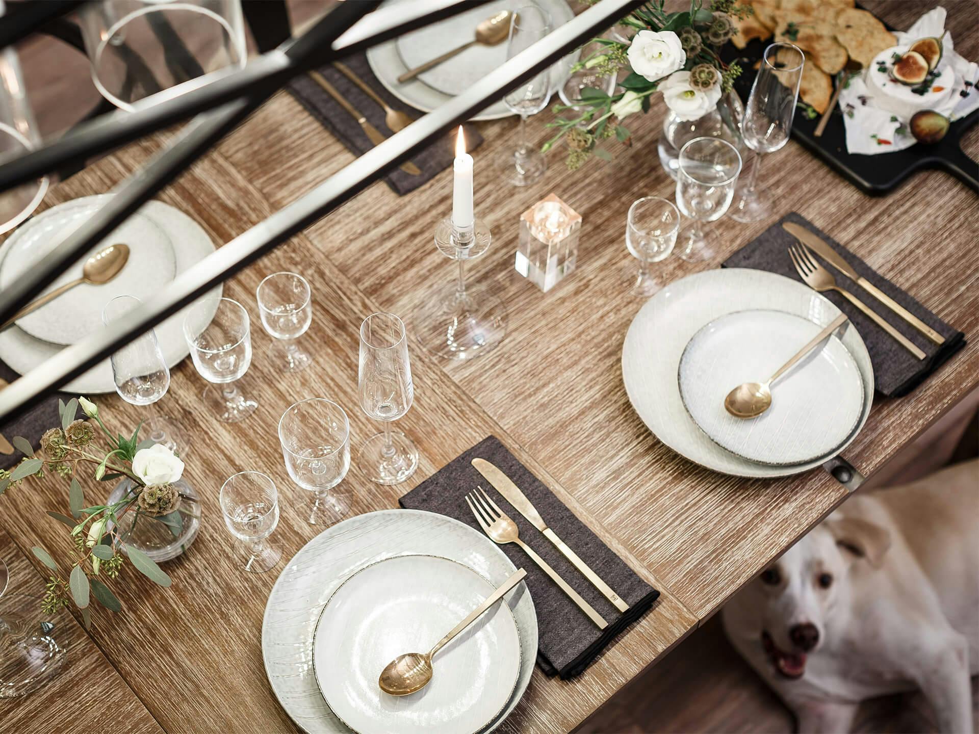 Lifestyle image of a wooden dinning room table that has been set with silverware and plates for a dinner