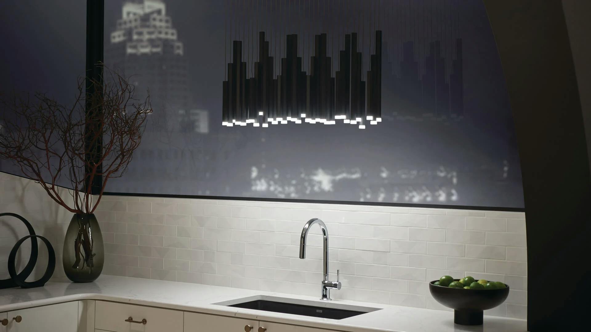 A high-rise kitchen at night featuring a cluster of soho pendants above a kitchen sink.