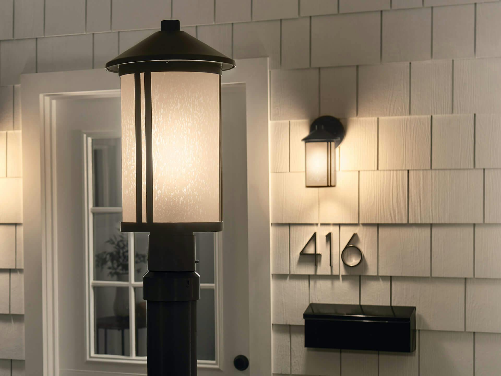 Exterior of a Lombard lamppost in black finish in front of a front door also featuring a Lombard sconce