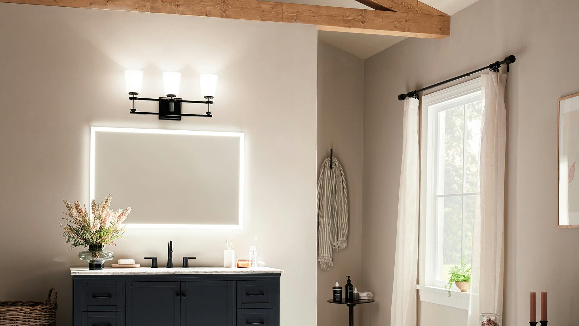 White bathroom with natural wood beams and dark vanity with Rosalind 3-light vanity light in black over mirror