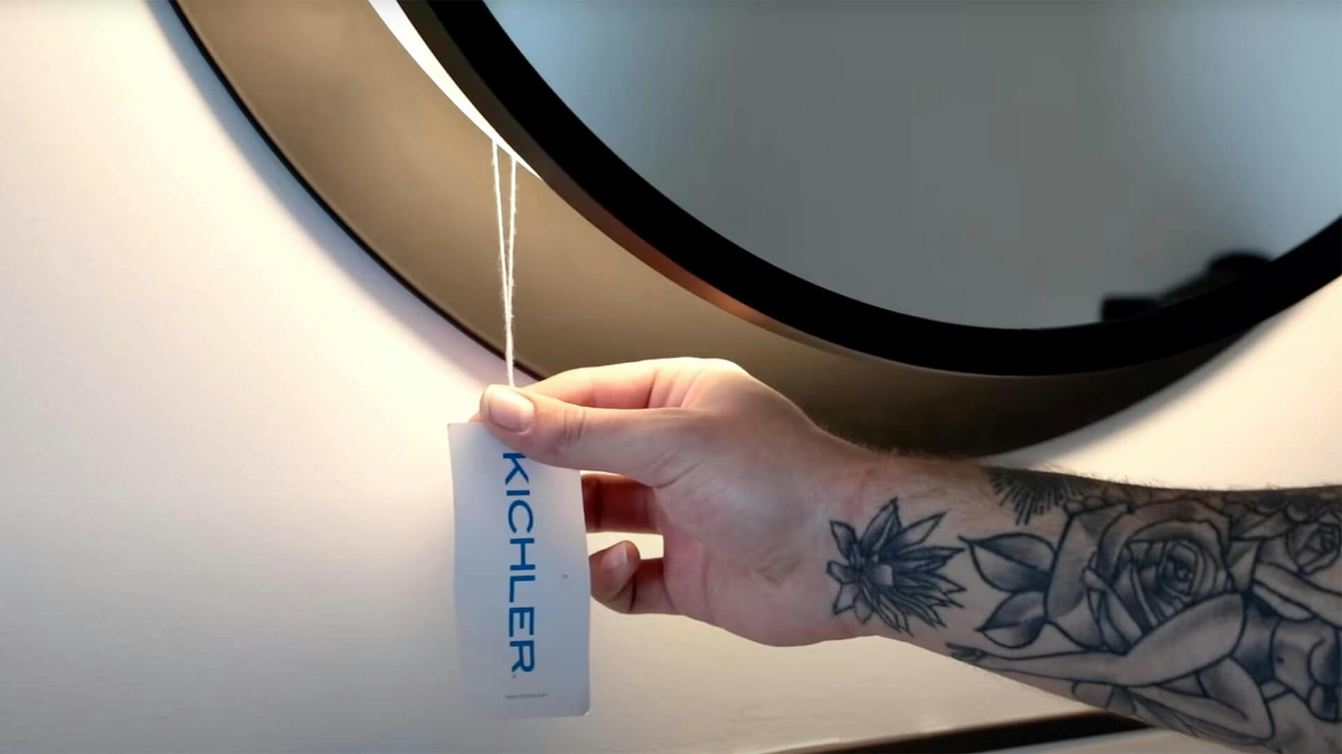 Close up of a tattooed hand holding a Kichler tag attached to a mirror with LED lights
