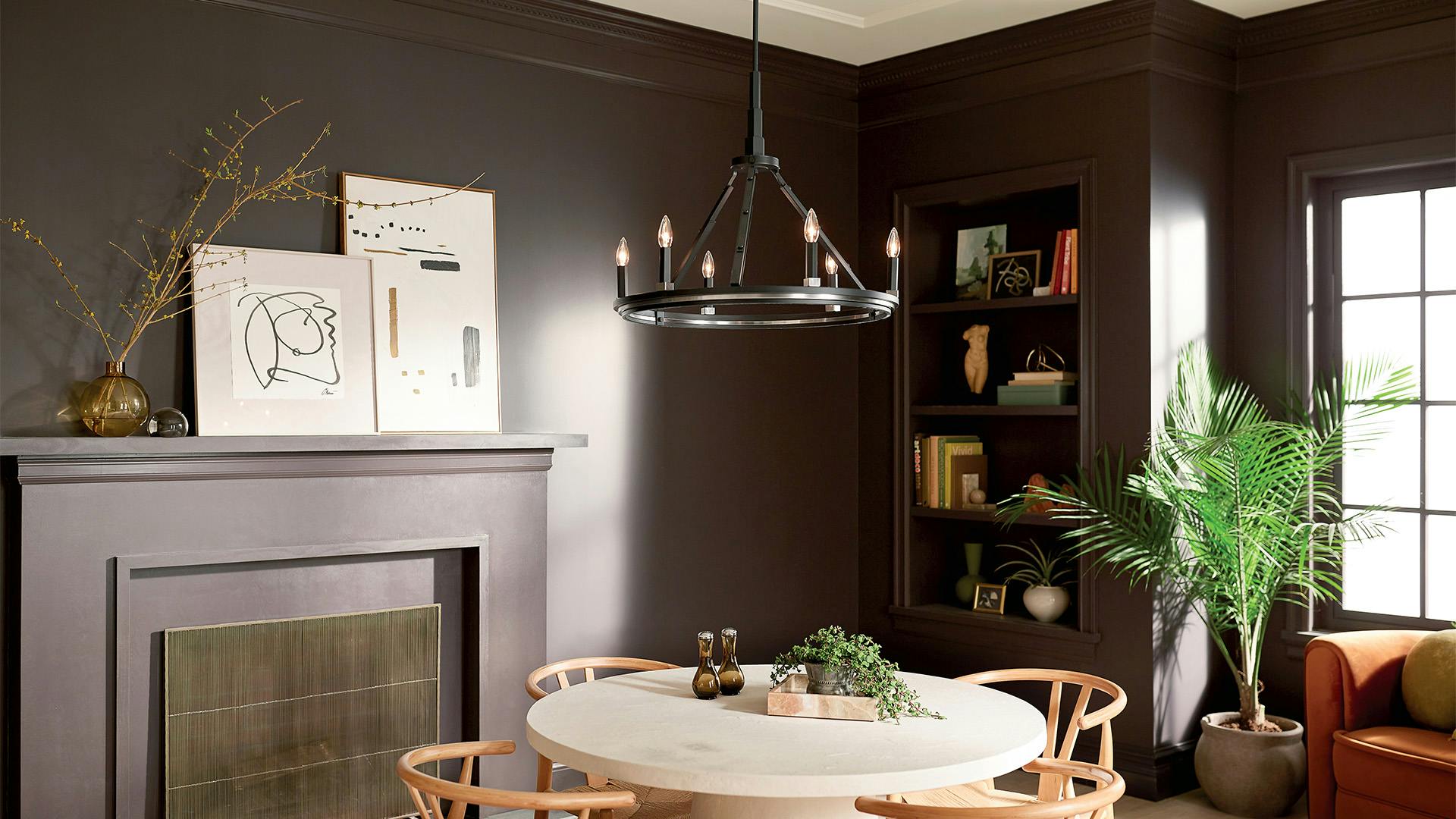 Dining room with dark brown walls and built in shelves with a black Emmala chandelier in the center