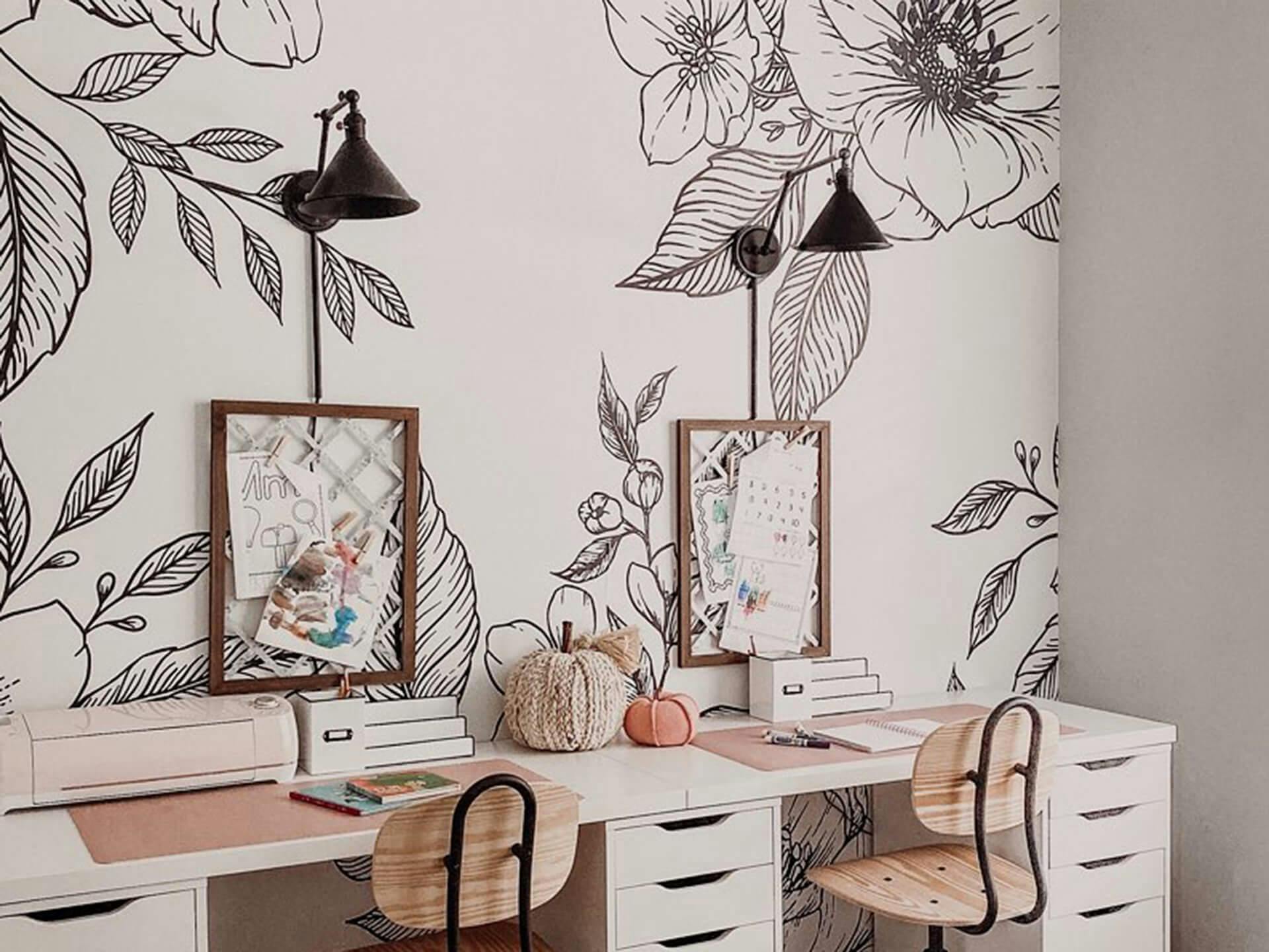 Office featuring a long desk with two workstations, an Ellerbeck sconce above each, against a white wall lined with a stenciled floral print