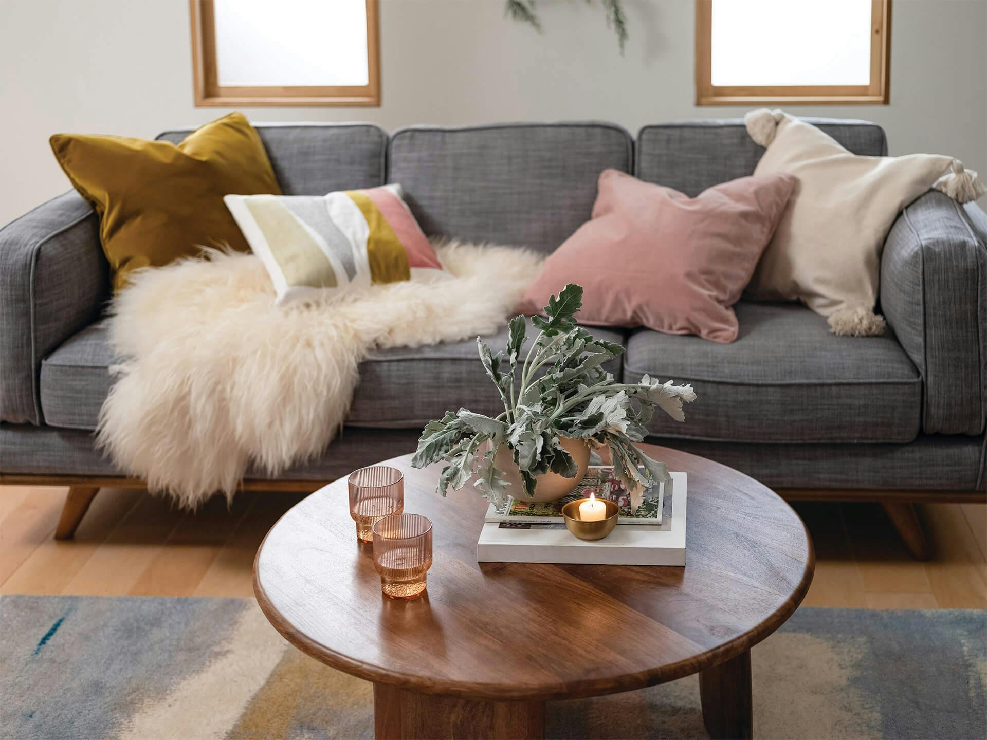 Living room setting, grey sofa with throw pillows and a round coffee table with plants and candle.